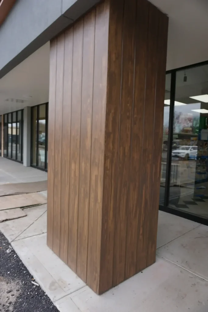 Close-up of a structural column wrapped in vertical dark walnut wood grain finish panels at a commercial retail storefront by Plaster Pro Stucco Contractors serving North Jersey