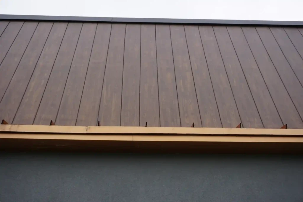 Upward close-up view of wood grain finish panel bracket and clip installation detail at the soffit transition by Plaster Pro Stucco Contractors serving North Jersey