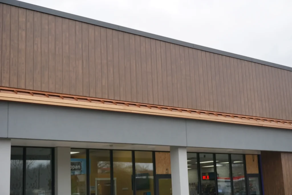 Wide view of commercial retail building with wood grain finish upper facade band above glazed storefront windows and white columns by Plaster Pro Stucco Contractors serving North Jersey
