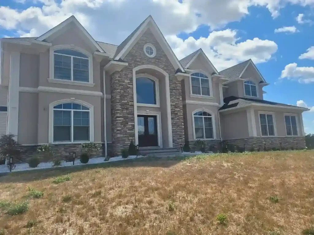 Wide front view of a luxury stucco home with stone facade center tower, multiple gabled dormers, and arched windows by Plaster Pro Stucco Contractors serving North Jersey