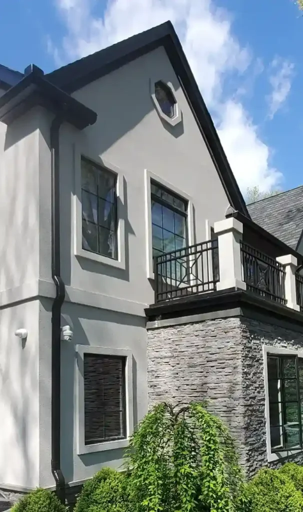 Luxury residential home corner view featuring stucco gable with octagonal window, iron balcony railing, and ledger stone facade lower section by Plaster Pro Stucco Contractors serving North Jersey