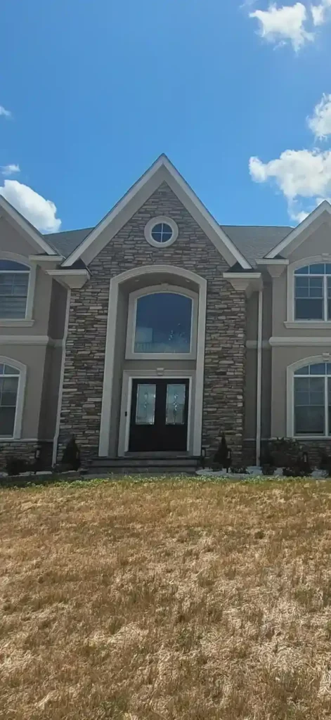 Two-story residential home with stucco exterior and stone facade accent on the center gable and entryway completed by Plaster Pro Stucco Contractors serving North Jersey