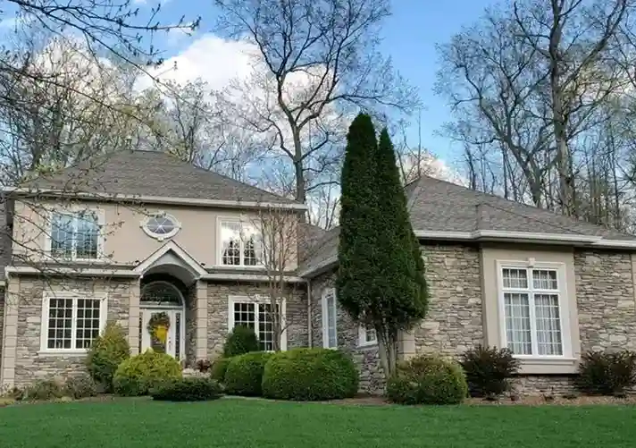 Two-story residential home with tan stucco upper exterior and full stone facade lower section with arched entryway by Plaster Pro Stucco Contractors serving North Jersey