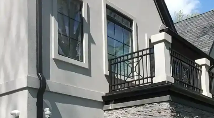 Luxury residential home corner view featuring stucco gable with octagonal window, iron balcony railing, and ledger stone facade lower section by Plaster Pro Stucco Contractors serving North Jersey